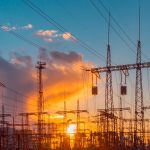 distribution electric substation with power lines and transformers, at sunset clouds